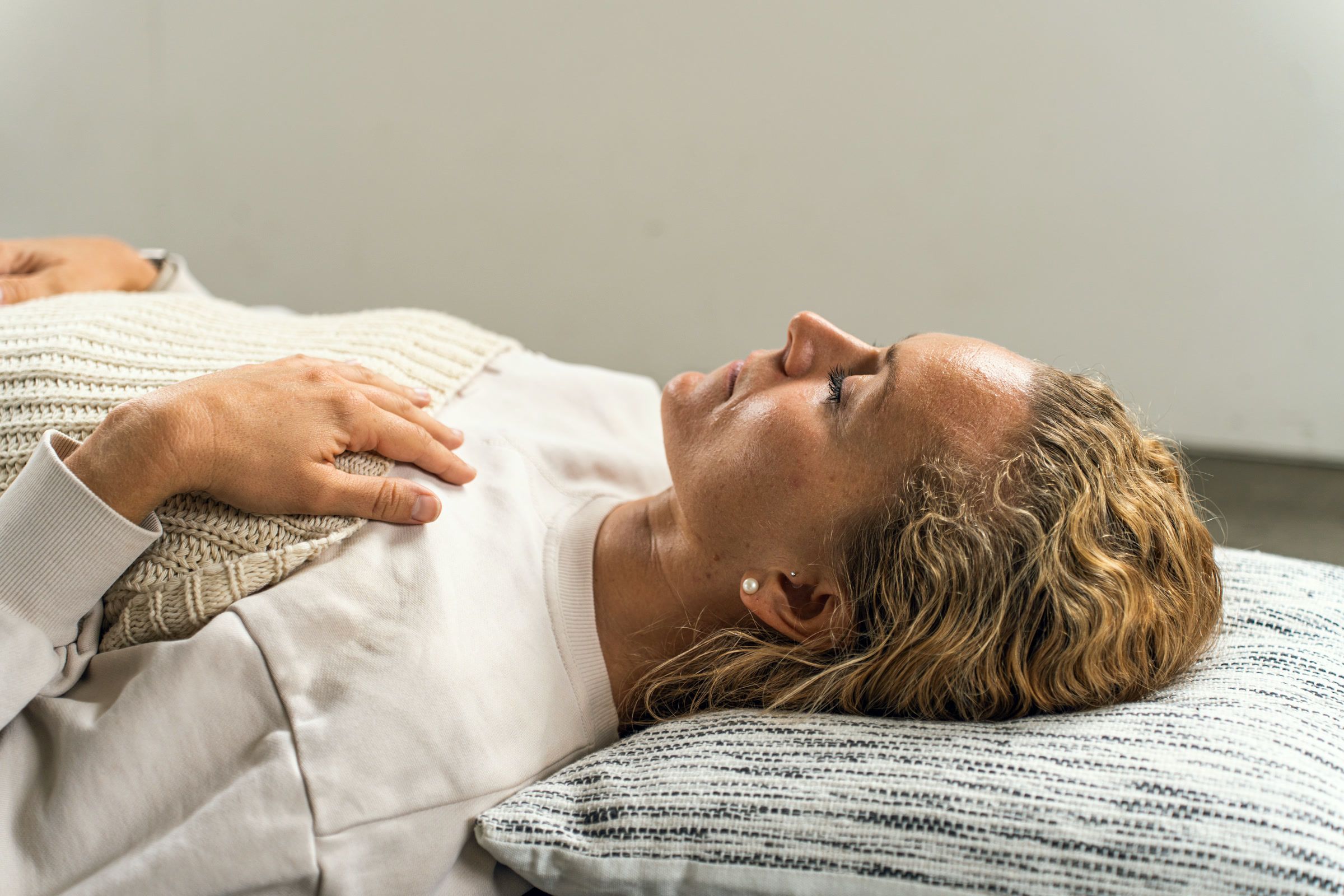 A woman lying on a mat with her eyes closed and one hand resting on her chest.