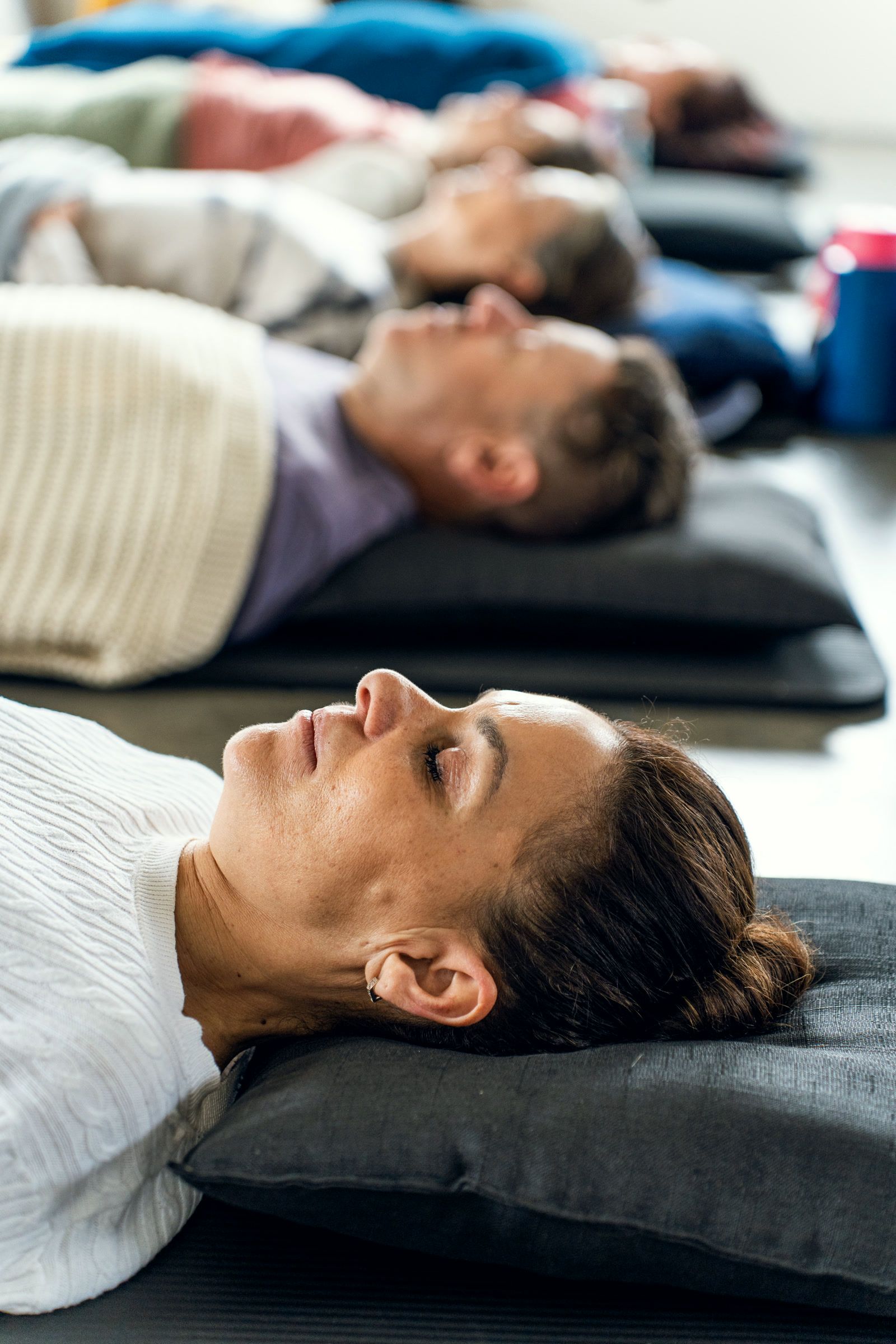 A row of people lying on mats with their eyes closed, mid-breath.